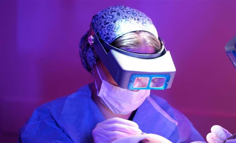Surgeon performing a hair transplant procedure in a purple-lit theatre